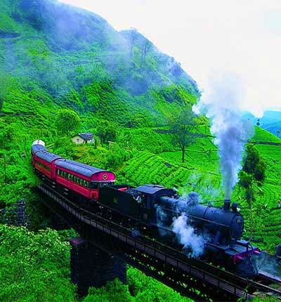 Steam locomotive train crossing bridge through lush green mountains in Nuwara Eliya, Sri Lanka